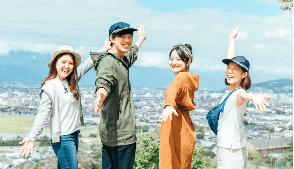 若者4人が見晴らしの良い丘の上で笑顔で手を広げている様子
